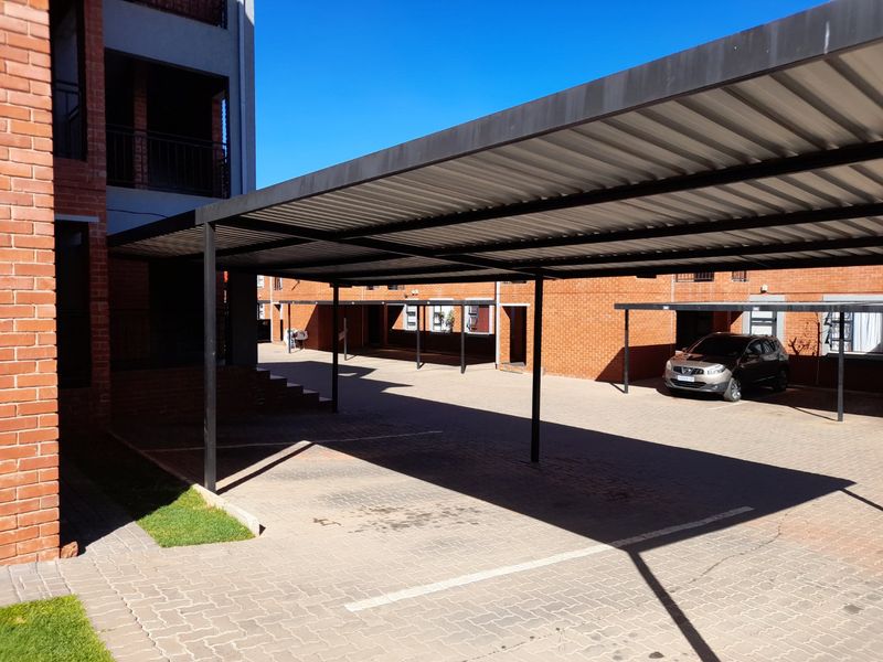 A well-maintained apartment complex parking area featuring covered carports with metal roofing and paved driveway surfaces.