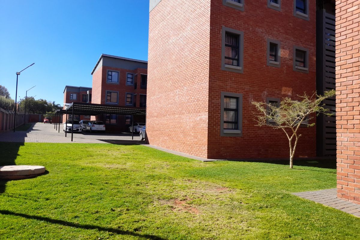 Exterior view of a modern face brick apartment complex featuring a well-maintained lawn and covered parking bays.