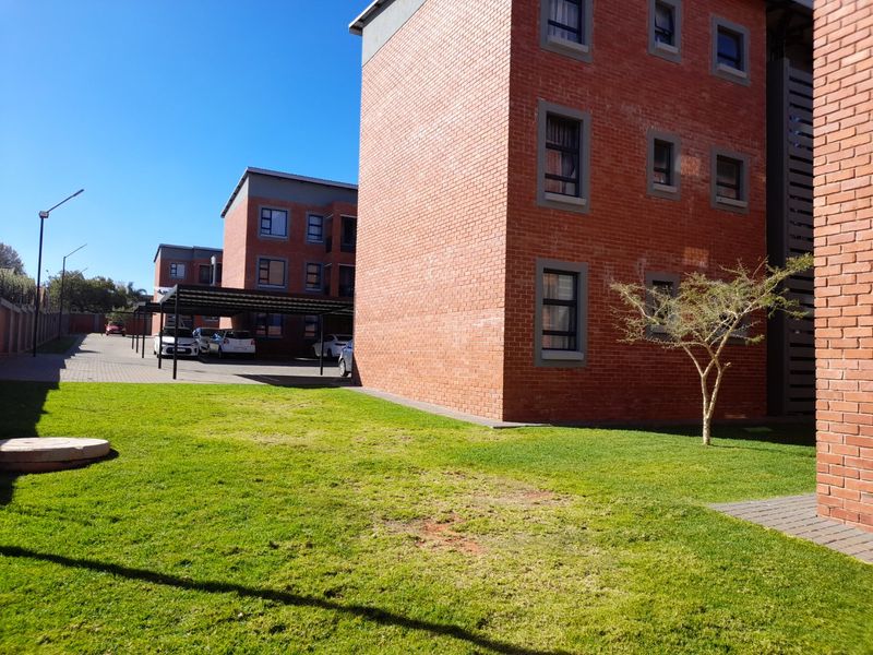 Exterior view of a modern face brick apartment complex featuring a well-maintained lawn and covered parking bays.