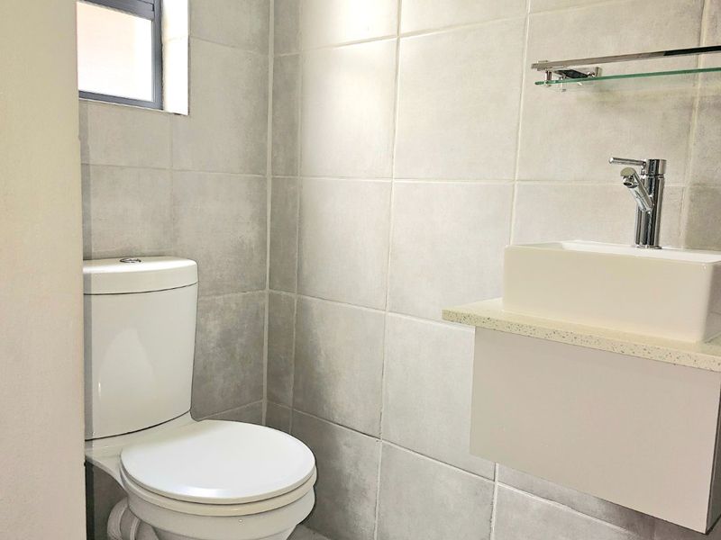 A clean and modern guest bathroom featuring neutral wall tiles, a wall-mounted vanity with a vessel sink, and a white toilet.