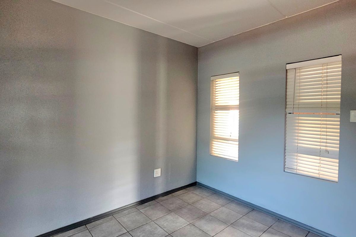 An empty bedroom featuring neutral grey walls, tiled flooring, and fitted venetian blinds, offering a clean and versatile space.