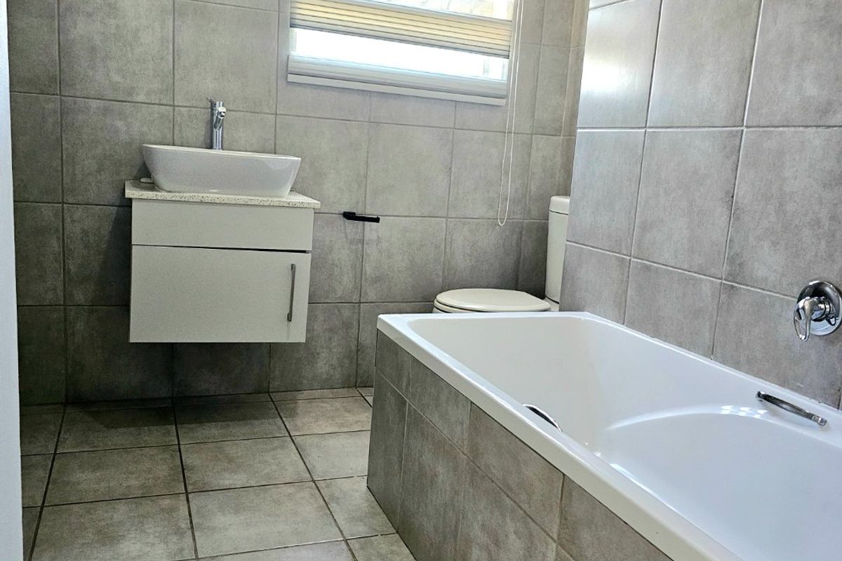 A modern, well-maintained bathroom featuring grey ceramic tiling, a wall-mounted vanity with a vessel sink, and a built-in bathtub.