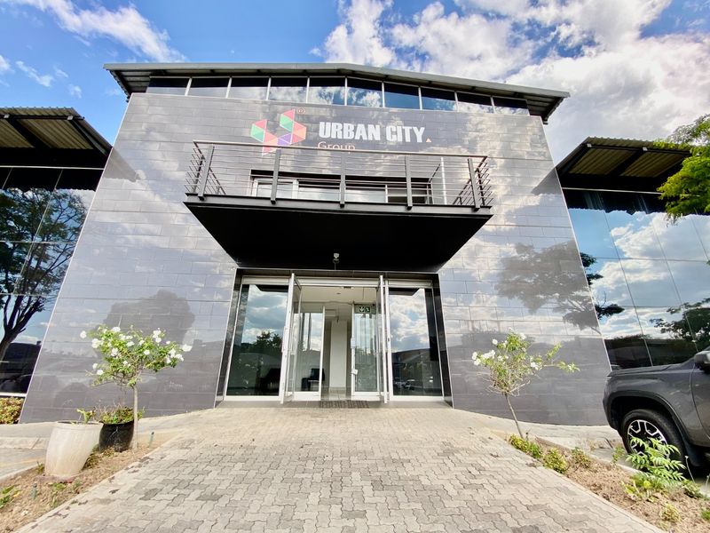 Modern industrial office building facade featuring dark tiled cladding, glass curtain walls, and a prominent entrance with a metal balcony.