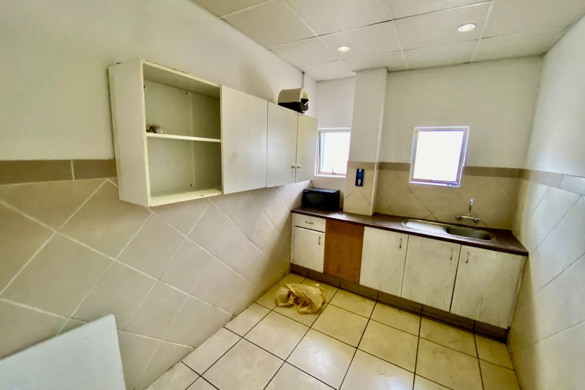 A functional kitchen area featuring built-in cabinetry, a stainless steel sink, tiled splashbacks, and recessed lighting in a drop ceiling.
