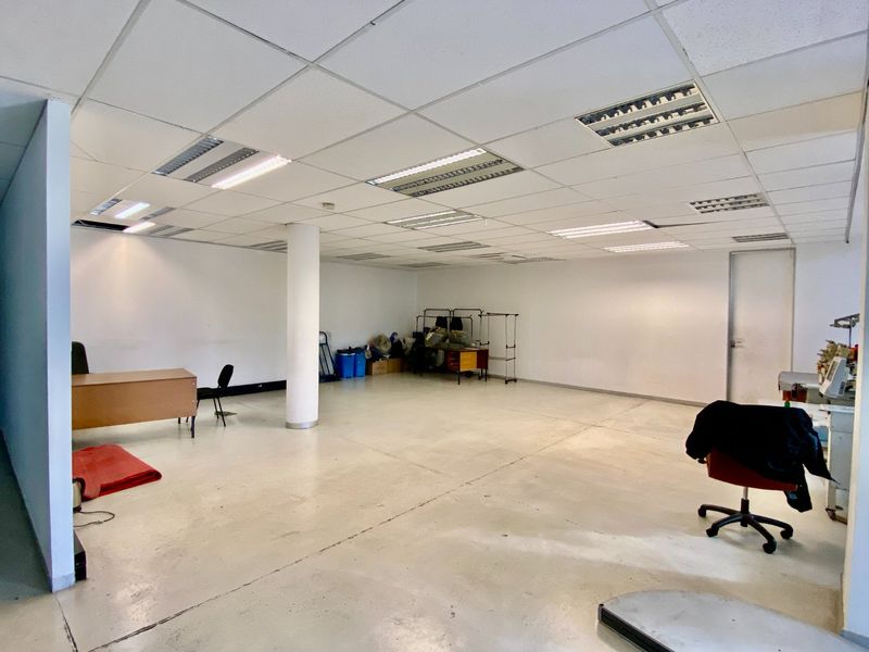Open-plan industrial office space featuring a suspended ceiling with recessed lighting, a central structural column, and durable painted concrete flooring.