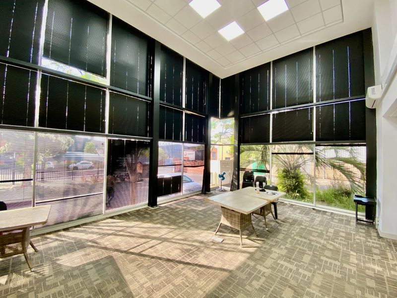 Spacious office area featuring high ceilings, extensive floor-to-ceiling windows with black frames, recessed lighting, and durable carpet tile flooring.
