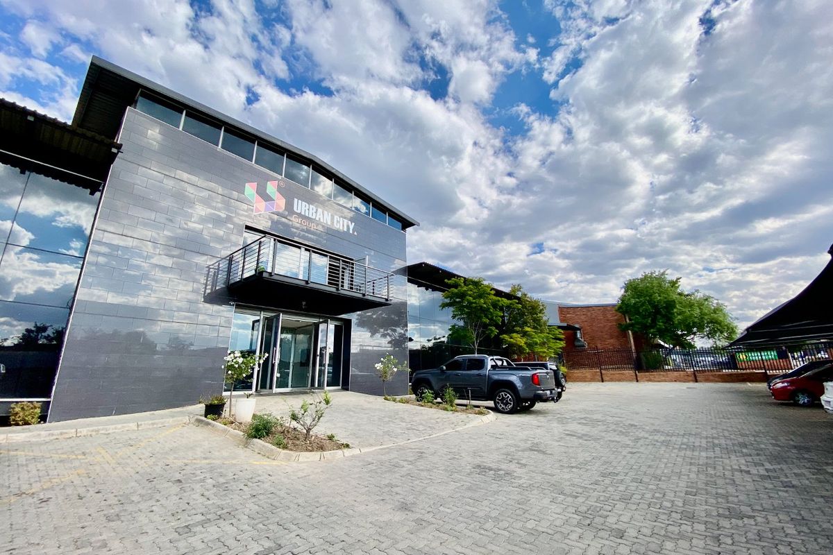 Modern industrial office building featuring a sleek tiled facade, glass curtain walling, and a private balcony, situated within a paved commercial complex.