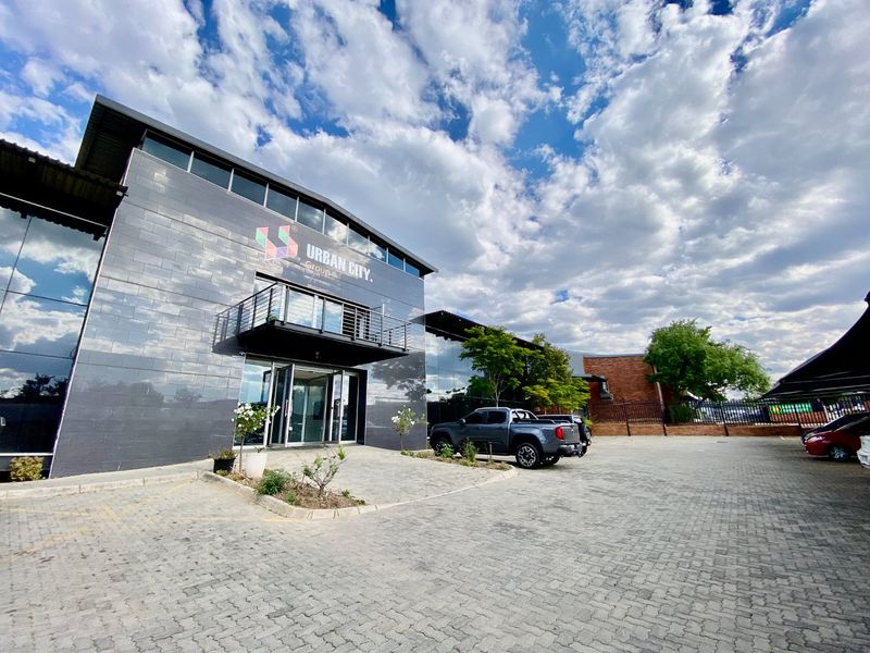 Modern industrial office building featuring a sleek tiled facade, glass curtain walling, and a private balcony, situated within a paved commercial complex.