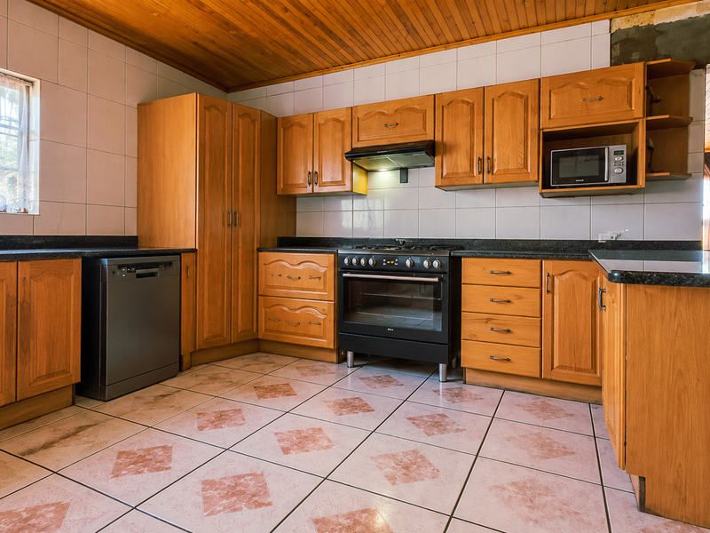 A functional kitchen featuring wooden cabinetry, granite countertops, built-in appliances, and tiled finishes, with an unfinished wall section above the upper cabinets.