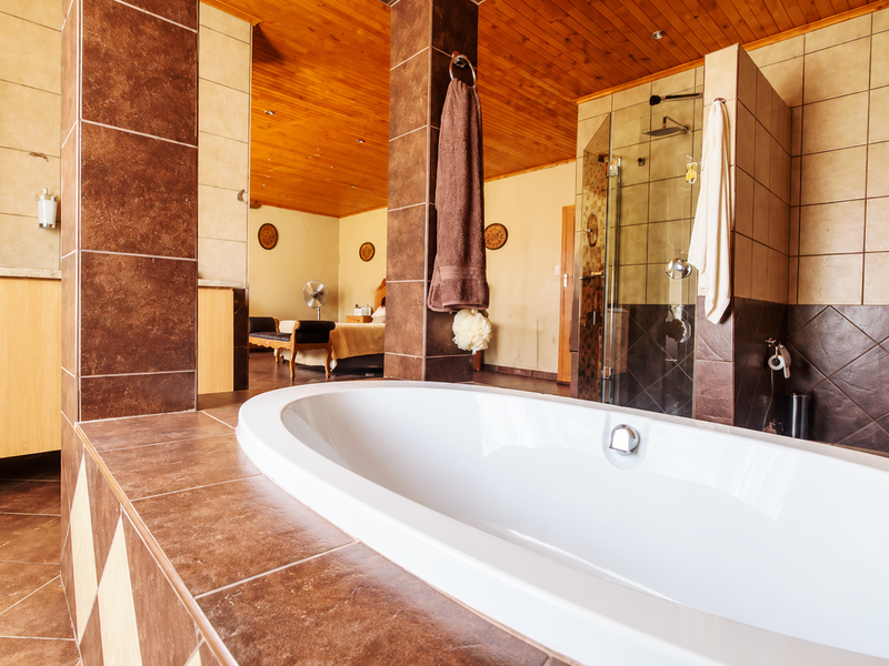 Spacious open-plan bathroom featuring a large oval bathtub, glass-enclosed shower, built-in vanity, and warm timber ceiling finishes.