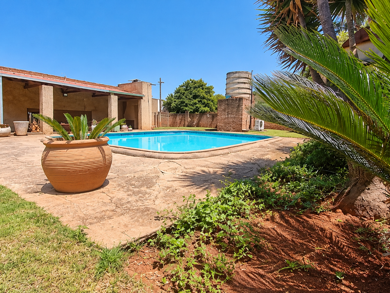 Outdoor pool area featuring a swimming pool, covered patio space, and a water tank, set within a landscaped garden with paved surrounds.