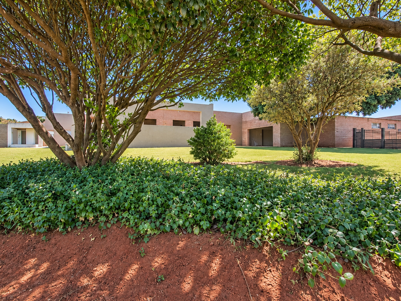 A well-maintained single-story brick house featuring a spacious front garden with mature trees and a secure gated entrance.
