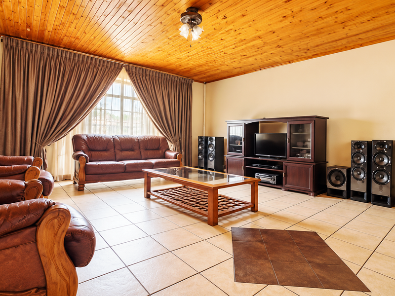 Spacious living room featuring a warm timber tongue and groove ceiling and neutral ceramic floor tiles, offering a comfortable and traditional living space.