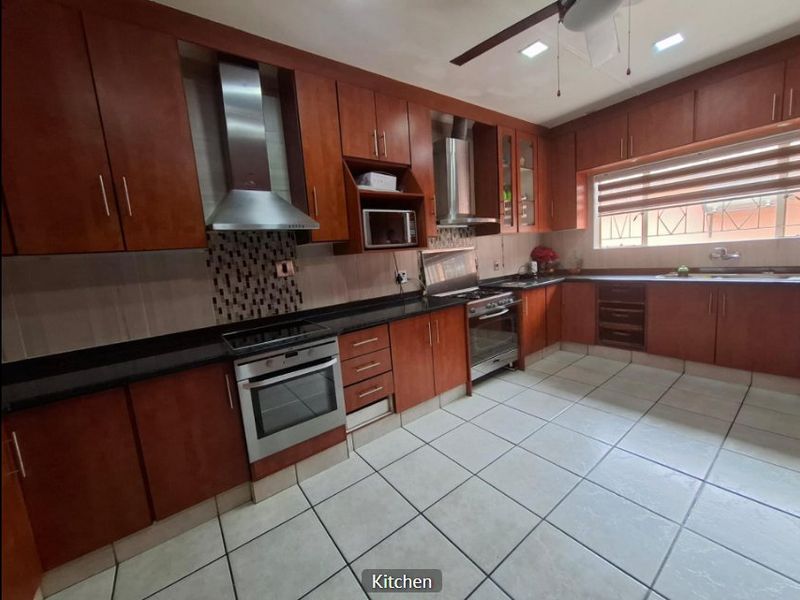 Spacious kitchen featuring warm-toned wooden cabinetry, granite countertops, stainless steel appliances, and tiled flooring with ample storage and workspace.