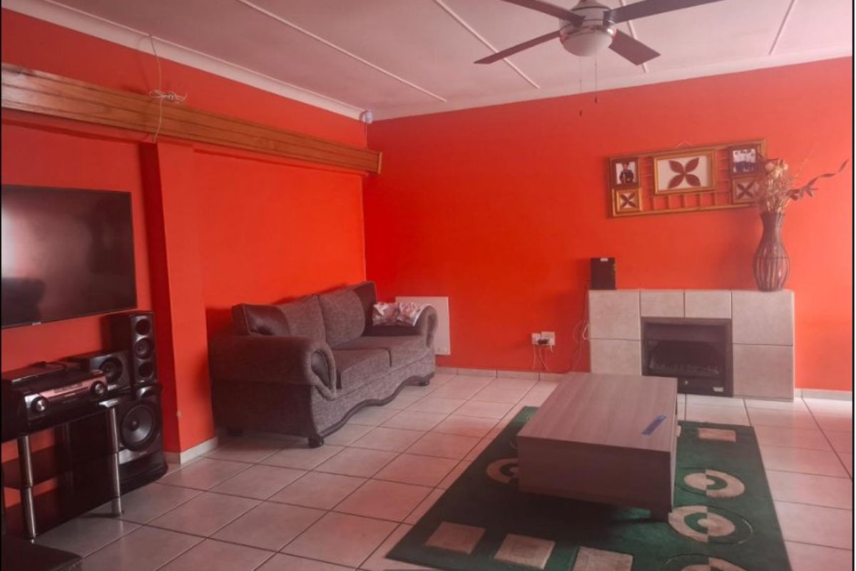 A living room featuring tiled flooring, a ceiling fan, and a built-in fireplace, finished with bright orange wall paint.