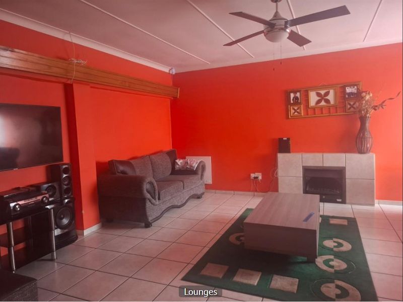 A living room featuring tiled flooring, a ceiling fan, and a built-in fireplace, finished with bright orange wall paint.
