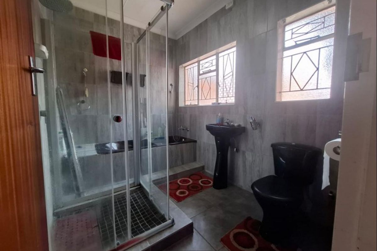 A functional bathroom featuring a glass shower enclosure, built-in bathtub, pedestal basin, and toilet, finished with modern grey wall tiles.