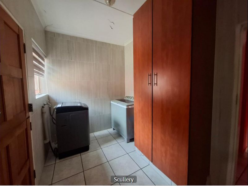 A functional laundry room featuring tiled walls and flooring, with a built-in storage cupboard and dedicated plumbing connections for appliances.