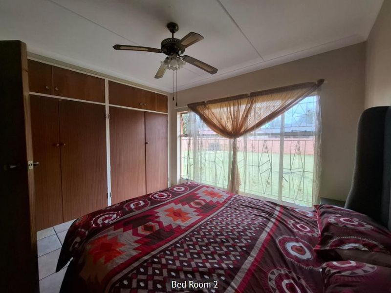 Bedroom featuring built-in wooden cupboards, a ceiling fan, and tiled flooring, with large windows fitted with security bars.
