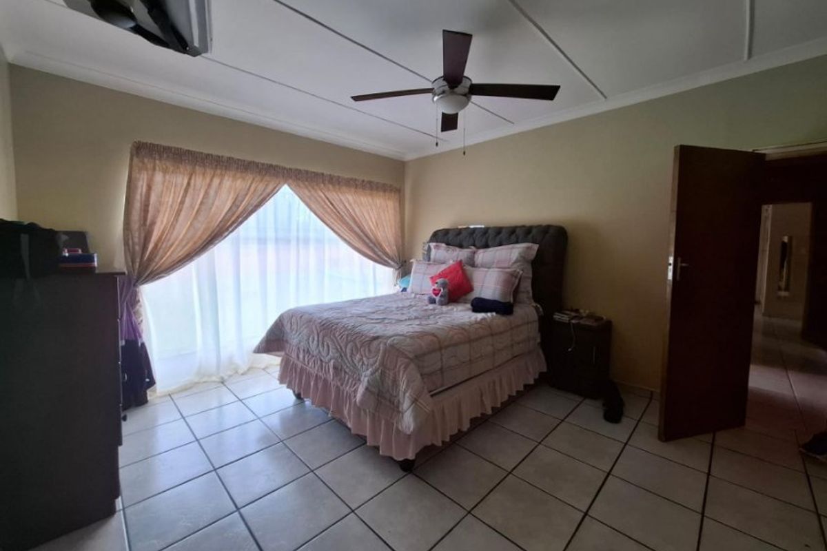 A spacious bedroom featuring tiled flooring, a ceiling fan, and a large sliding glass door that provides natural light.