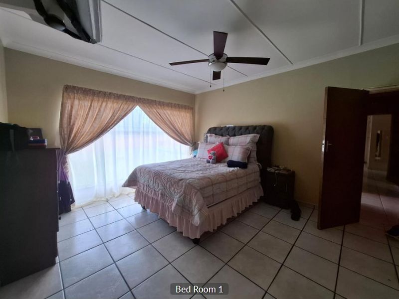 A spacious bedroom featuring tiled flooring, a ceiling fan, and a large sliding glass door that provides natural light.