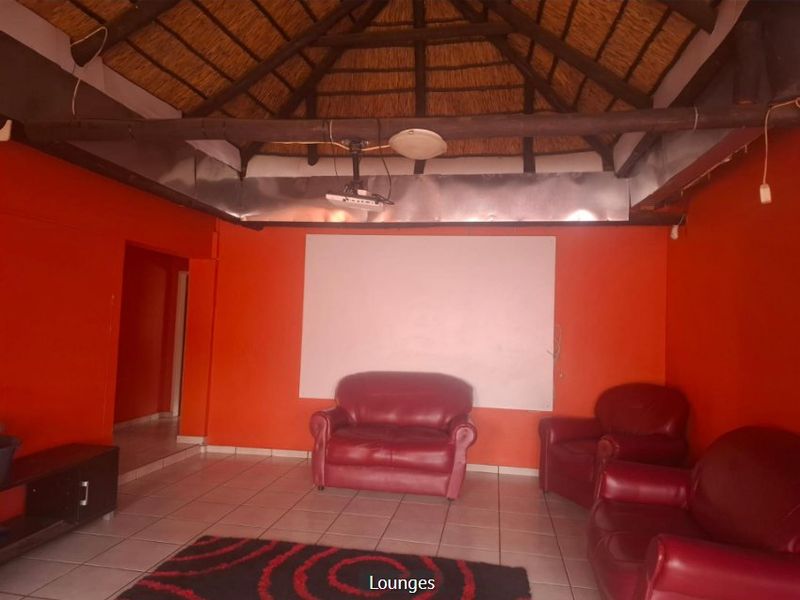 Living room featuring a traditional thatched roof with exposed timber beams, tiled flooring, and a built-in projector setup.