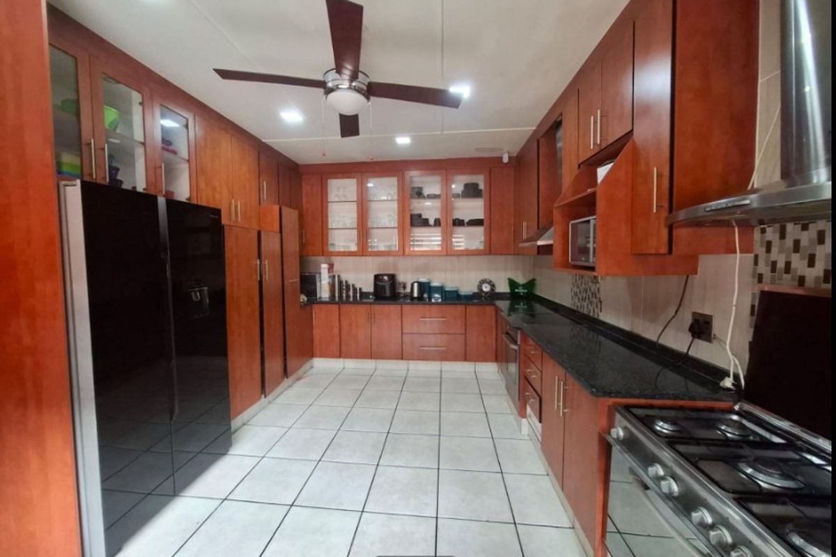 A well-appointed kitchen featuring extensive wooden cabinetry, granite countertops, a gas hob with extractor, and tiled flooring with recessed lighting.