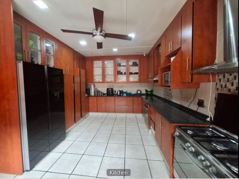 A well-appointed kitchen featuring extensive wooden cabinetry, granite countertops, a gas hob with extractor, and tiled flooring with recessed lighting.