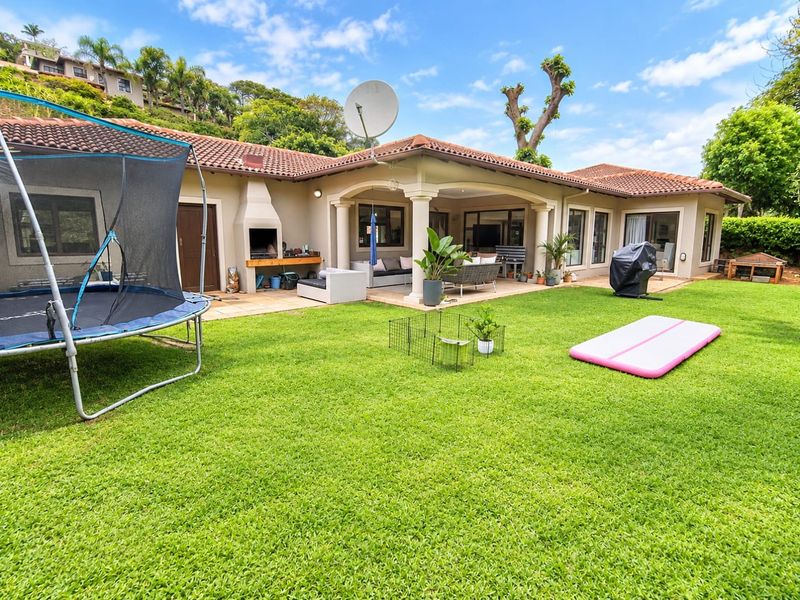 Spacious rear garden featuring a well-maintained lawn and a covered patio area with a built-in braai, perfect for outdoor entertaining.