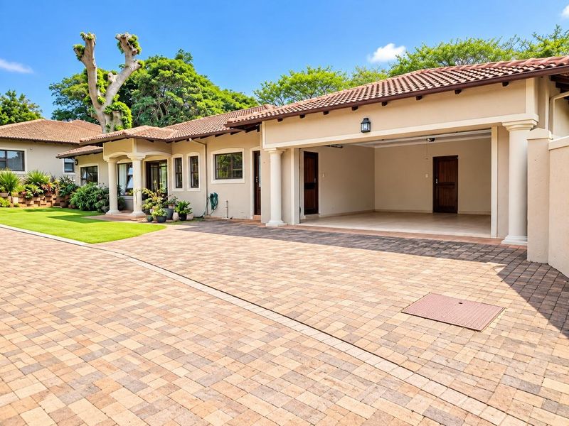 A well-maintained townhouse exterior featuring a spacious paved driveway, a double garage, and a neatly landscaped front lawn with classic architectural columns.