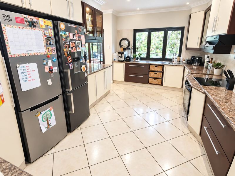 A well-maintained kitchen featuring granite countertops, ample built-in cabinetry, integrated appliances, and ceramic tile flooring with a large window providing natural light.
