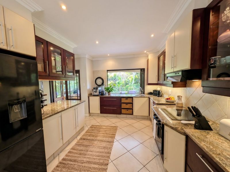 A well-appointed kitchen featuring granite countertops, fitted cabinetry, built-in oven, electric hob, and a large window overlooking the garden.
