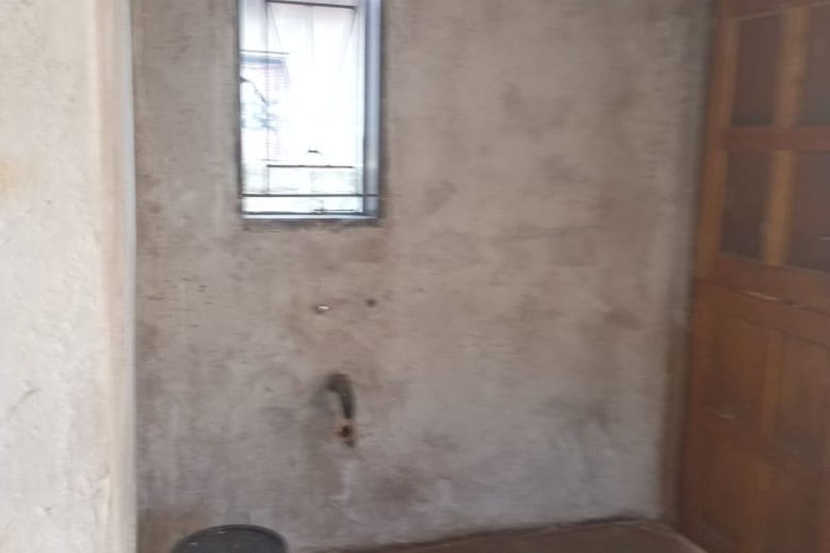 An unfinished utility or laundry space featuring exposed plaster walls, concrete flooring, and plumbing connections ready for installation.