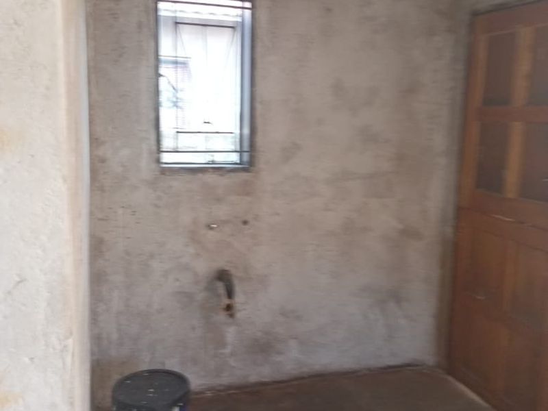 An unfinished utility or laundry space featuring exposed plaster walls, concrete flooring, and plumbing connections ready for installation.