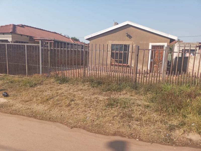 Front view of a single-story residential house featuring a tiled roof, plastered exterior walls, and secure metal perimeter fencing.