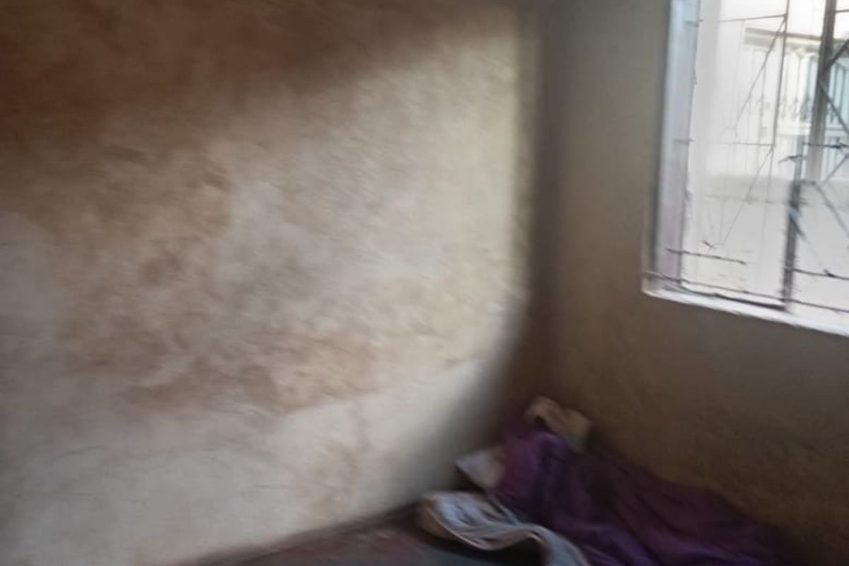 A sparse bedroom featuring a window with security bars, requiring significant wall repairs and cosmetic updates to improve the living space.