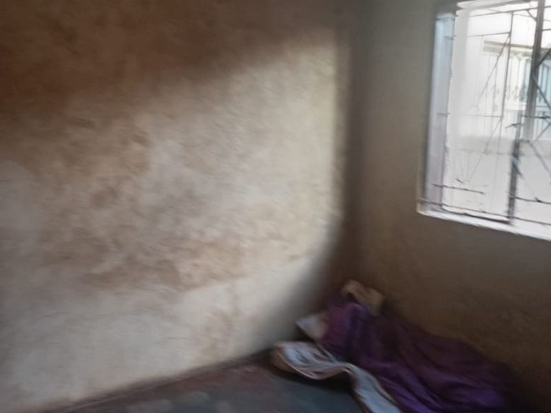 A sparse bedroom featuring a window with security bars, requiring significant wall repairs and cosmetic updates to improve the living space.