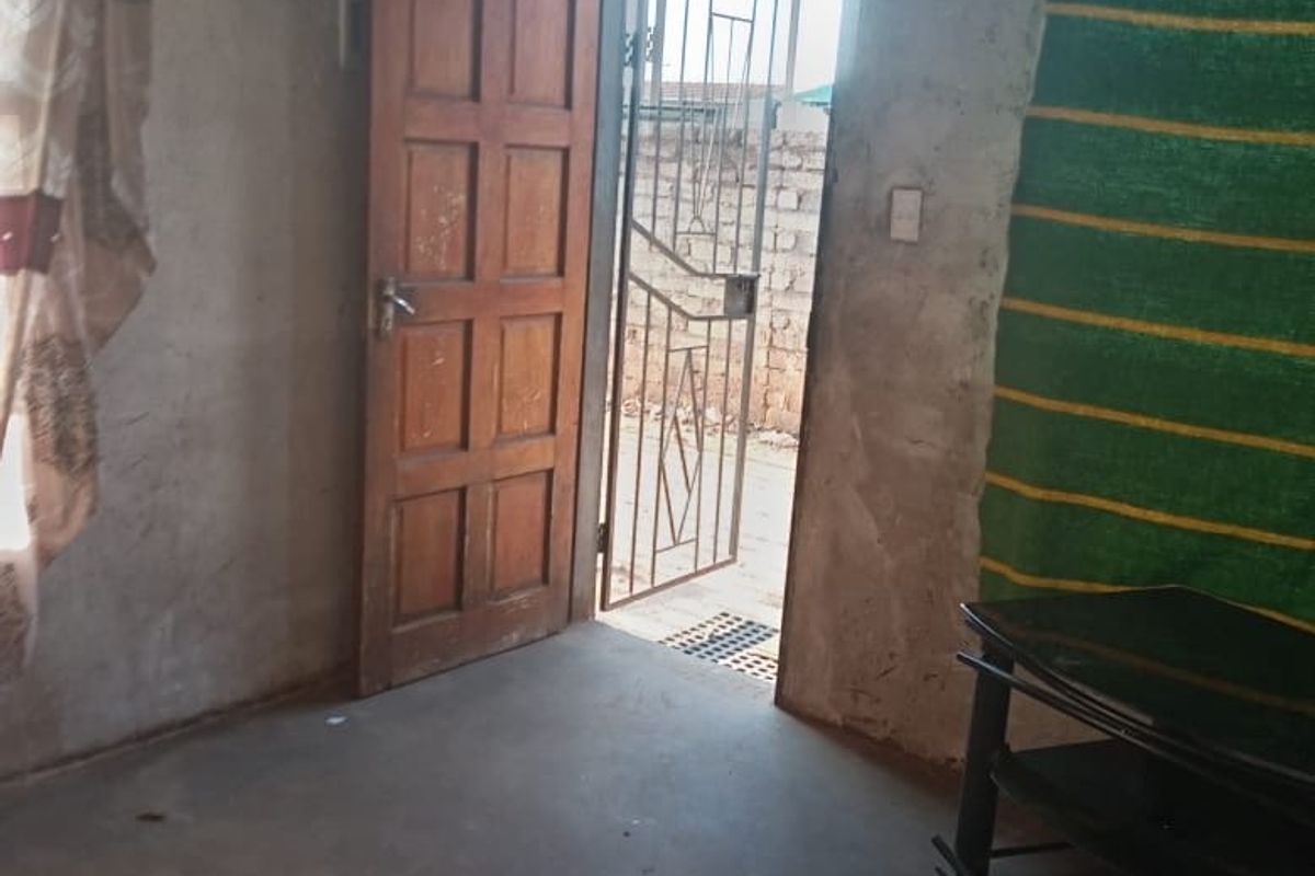 An interior living space featuring unfinished concrete walls, a timber door, and a security gate leading to the exterior.