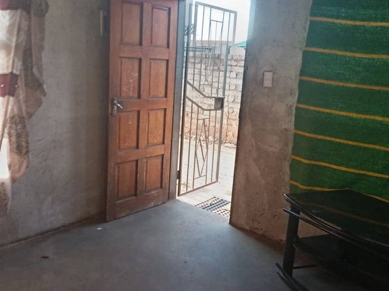An interior living space featuring unfinished concrete walls, a timber door, and a security gate leading to the exterior.