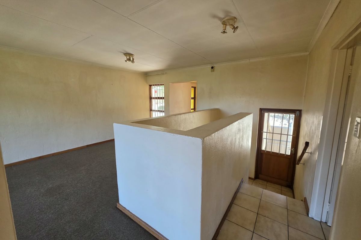 An empty, open-plan living area featuring a staircase landing, carpeted flooring, and direct access to an exterior door with security gate.