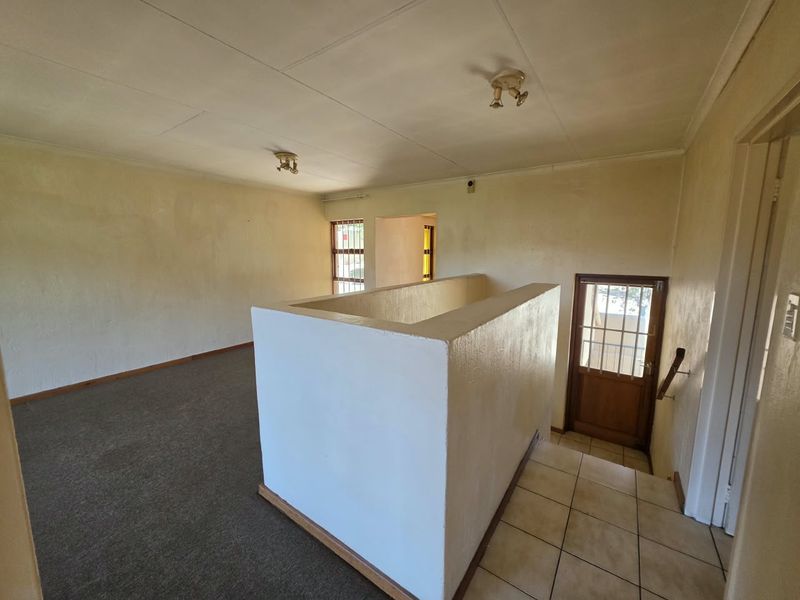 An empty, open-plan living area featuring a staircase landing, carpeted flooring, and direct access to an exterior door with security gate.