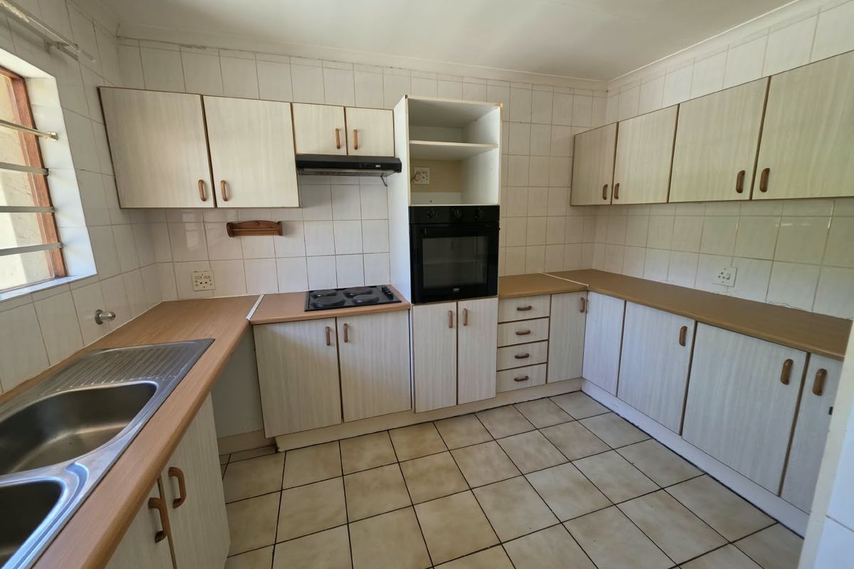 A functional kitchen featuring laminate countertops, built-in oven, electric hob, extractor fan, and ample cabinetry, finished with tiled splashbacks and ceramic flooring.