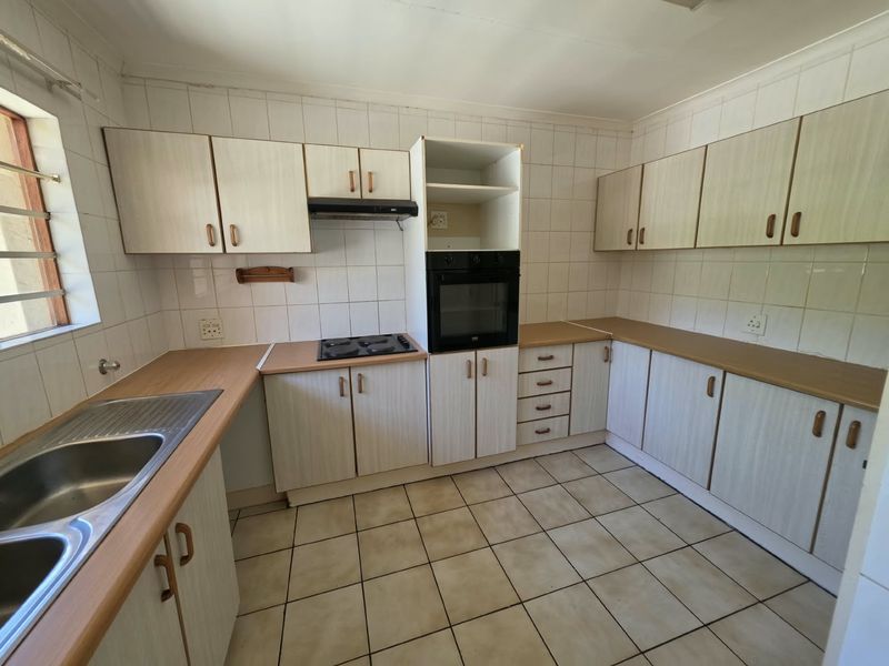 A functional kitchen featuring laminate countertops, built-in oven, electric hob, extractor fan, and ample cabinetry, finished with tiled splashbacks and ceramic flooring.