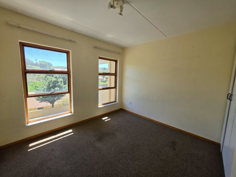 An empty bedroom featuring carpeted flooring, built-in cupboards, and large windows providing natural light and exterior views.