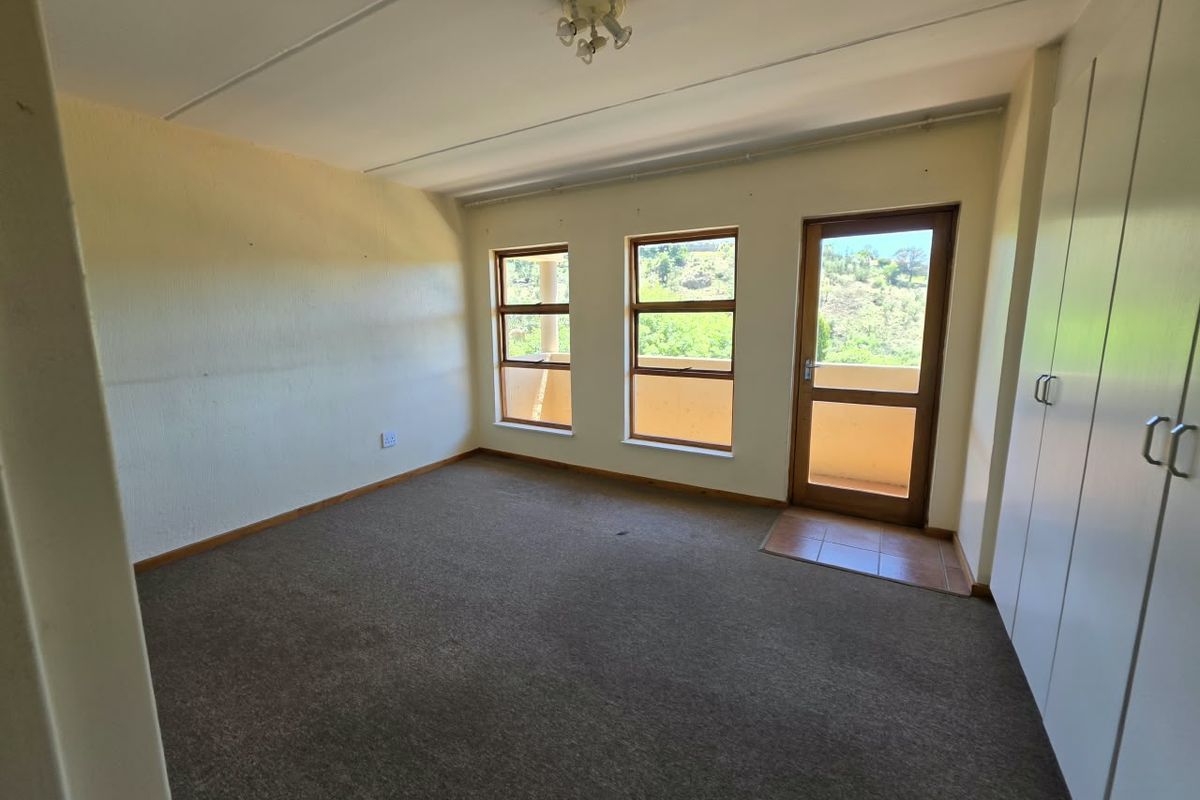 An empty bedroom featuring built-in cupboards, carpeted flooring, and direct access to an outdoor balcony area through a timber-framed door.
