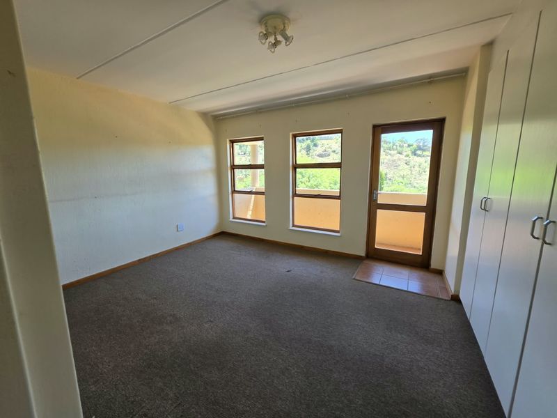 An empty bedroom featuring built-in cupboards, carpeted flooring, and direct access to an outdoor balcony area through a timber-framed door.