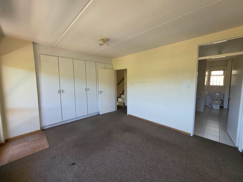 An empty bedroom featuring built-in cupboards, carpeted flooring, and an adjacent bathroom, offering a blank canvas for renovation and interior design updates.