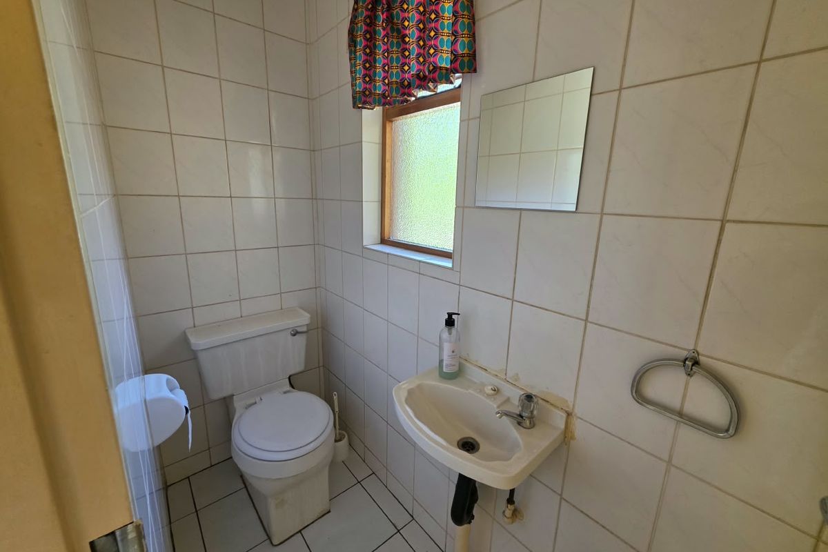 A compact bathroom featuring a standard toilet, pedestal basin, and full-height wall tiling, requiring cosmetic updates to modernize the space.