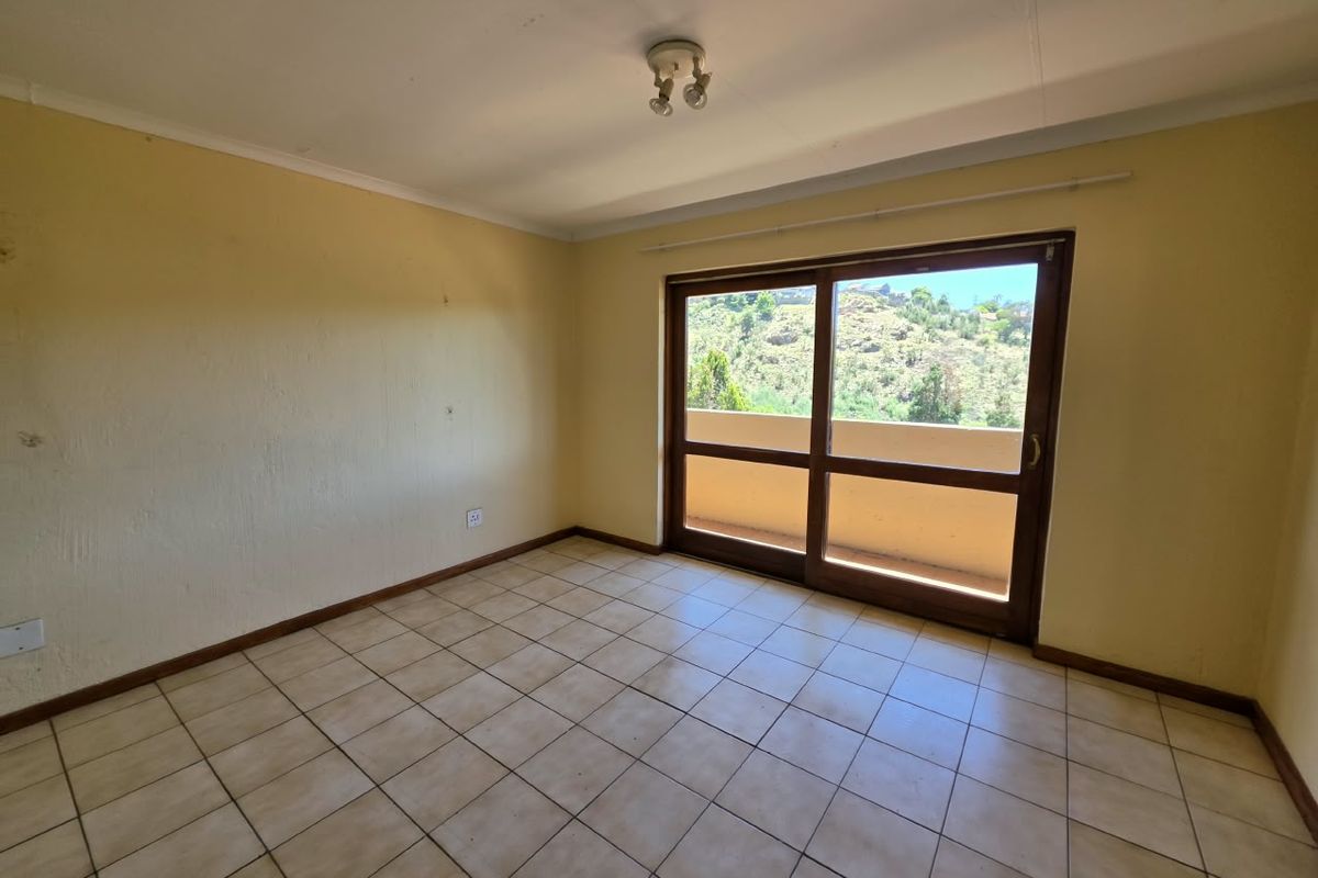 An empty bedroom featuring tiled flooring and a sliding glass door that opens onto a balcony with scenic views.
