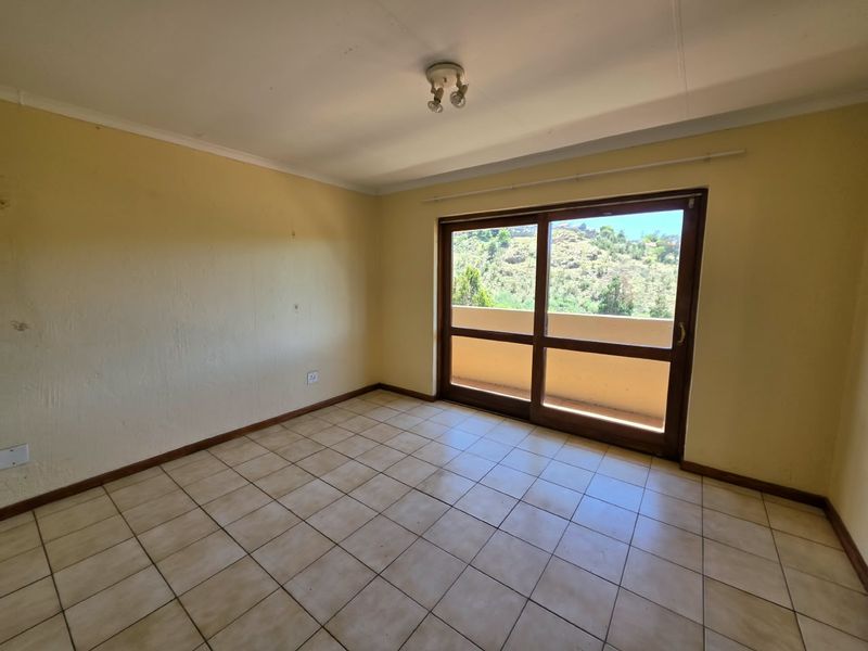 An empty bedroom featuring tiled flooring and a sliding glass door that opens onto a balcony with scenic views.